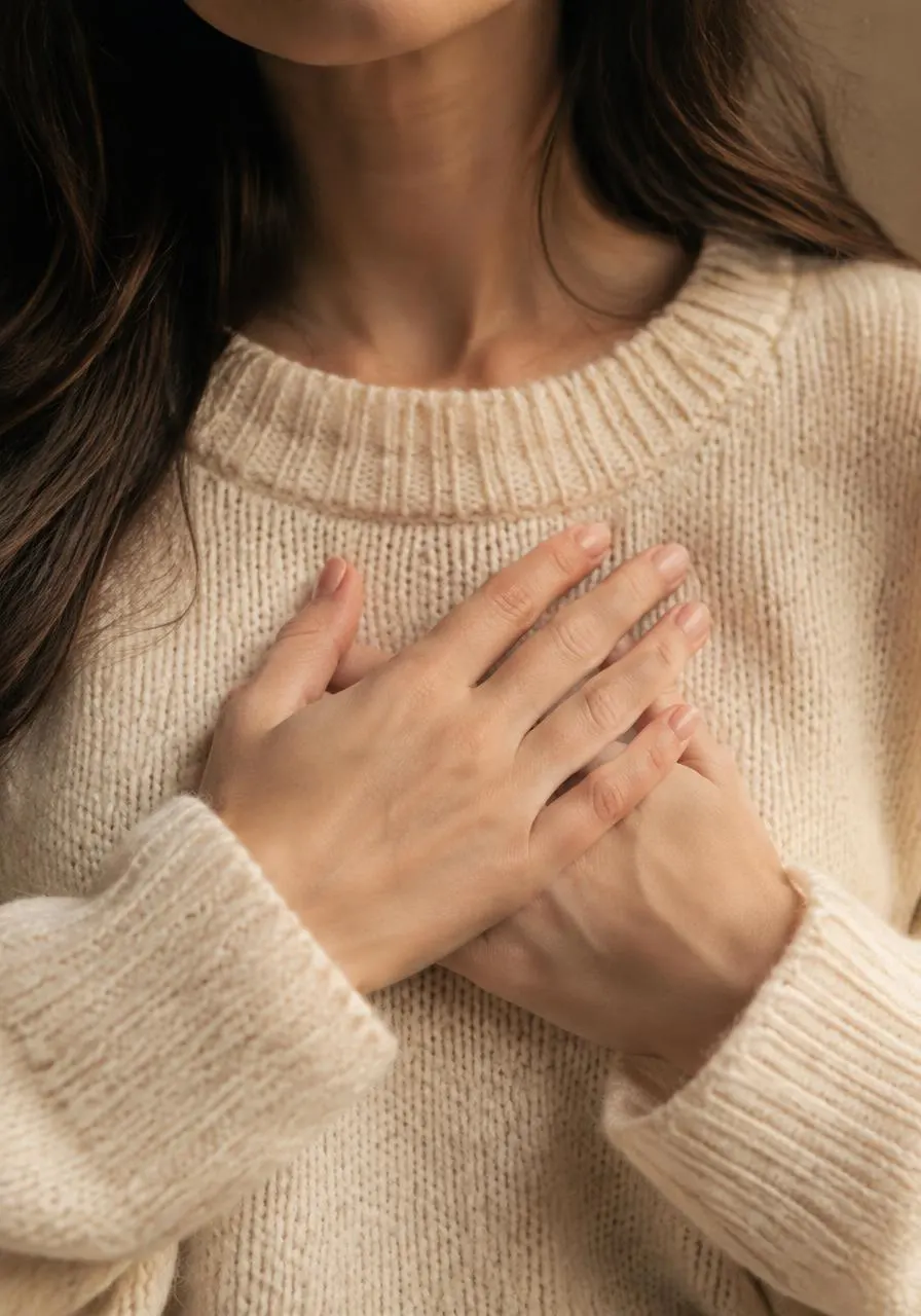 Hands resting over the heart on a soft knit sweater